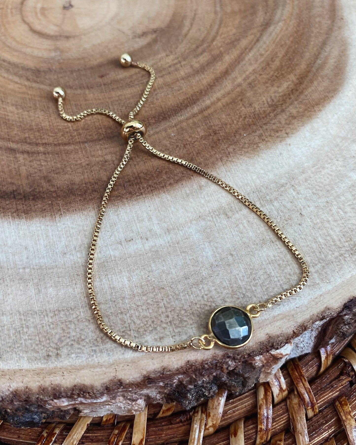 Gold bracelet with a dark silver stone on a wooden surface