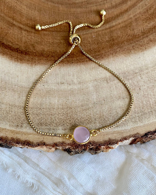 Gold bracelet with a pink gemstone on a wooden surface